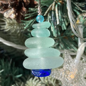 Könnte beinhalten: Ein blaugrüner und weißer Weihnachtsbaumschmuck aus Glas. Der Schmuck besteht aus fünf übereinander gestapelten Teilen aus Meerglas, mit einem blauen Glasstern am Boden.