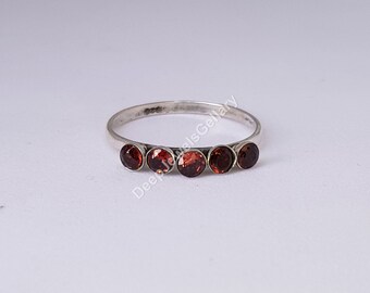 Può includere: Un anello d'argento con cinque pietre preziose rotonde, di un rosso intenso, disposte in fila. Le pietre sono uniformemente distanziate lungo la fascia, creando una linea continua di colore. Sfondo bianco.