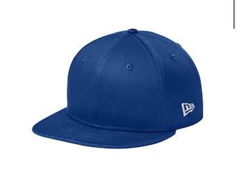 Könnte beinhalten: Eine einfarbige, königsblaue Baseballkappe mit strukturierter Krone und flachem Schirm. Die Kappe hat ein kleines, weiß gesticktes Logo an der Seite. Das Design besteht aus sechs Paneelen mit genähten Ösen und einem Knopf in der Mitte oben.