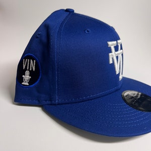May include: A royal blue baseball cap with a white "LA" logo on the front and a black circle with a microphone and the word "VIN" on the side.
