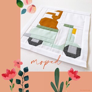 Könnte beinhalten: Ein weißer Stoffblock mit einem Patchwork-Design eines grün-gelben Mopeds. Das Moped hat einen braunen Sitz und ein schwarz-graues Rad. Der Stoffblock hat das Wort "moped" in orange unter dem Moped geschrieben.