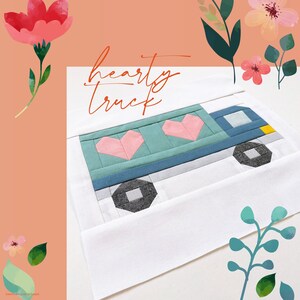 May include: A white fabric square with the text "hearty truck" printed in black. A blue truck with a green bed and pink hearts is appliqued on the fabric. The truck has a yellow detail on the front and black wheels.