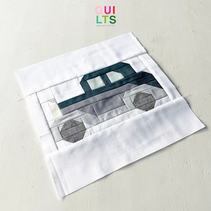 May include: A quilt block featuring a patchwork car design in shades of gray and teal. The car is outlined in white and has a white windshield. The quilt block is on a white background.