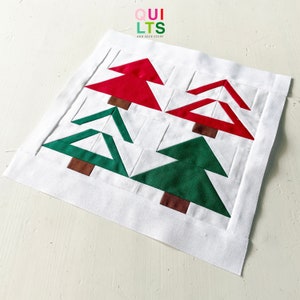 May include: A white fabric square with four appliquéd Christmas trees. Two trees are red and two are green. The trees are made of fabric and have a brown fabric trunk.