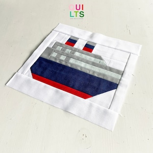Pode incluir: Um quadrado de tecido branco com uma aplicação de navio azul e cinza. O navio tem detalhes vermelhos e é contornado em branco. O quadrado de tecido tem o texto "QUILTS AND NICE STUFF" no canto superior esquerdo.