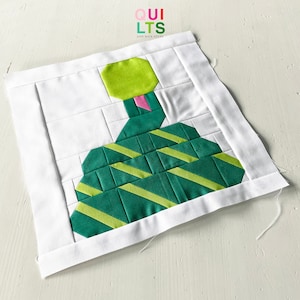 May include: A green and yellow geometric quilt block with the text "QUILTS AND NICE STUFF" in the top left corner. The block is made up of squares and triangles, and it is sewn together with a white background.