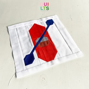 May include: A white fabric square with a red, blue, and gray geometric design. The design is a stylized image of a canoe with a paddle.