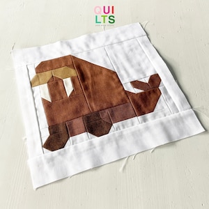 Könnte beinhalten: Ein brauner und weißer Patchwork-Quiltblock, der ein Walross darstellt. Der Block besteht aus verschiedenen Brauntönen und hat einen weißen Hintergrund. Der Quiltblock ist von einem weißen Rand umgeben.
