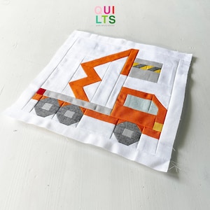 Puede incluir: Un cuadrado de tela blanco con un diseño de patchwork de un camión de construcción naranja con un brazo de grúa gris y amarillo. El camión tiene una cabina gris con una ventana azul claro y ruedas grises. El texto "QUI LTS AND NICE STUFF" está impreso en la esquina superior izquierda del cuadrado de tela.