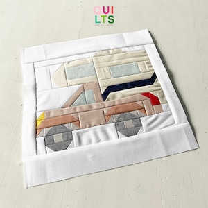 Może przedstawiać: Biały kwadratowy kawałek materiału z kolorowym patchworkowym wzorem przedstawiającym kampera. Materiał jest zszyty na krawędziach białym obramowaniem. W lewym górnym rogu nadrukowany jest tekst "QUI LTS AND NICE STUFF".