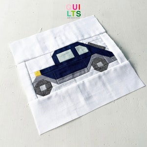 May include: A blue and gray patchwork car quilt block with a yellow detail. The block is on a white background.
