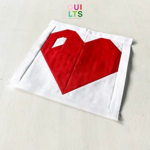 May include: A red heart-shaped quilt block on a white background. The block is made of several pieces of fabric sewn together. The text "QUILTS AND NICE STUFF" is visible in the top left corner of the image.