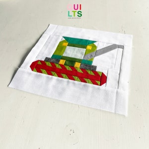 Könnte beinhalten: Ein grüner, gelber und grauer Patchwork-Quiltblock, der einen Traktor darstellt. Der Block ist auf einen weißen Hintergrund genäht, mit dem Text "QUI LTS AND NICE STUFF" in der oberen linken Ecke.