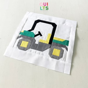 May include: A green, yellow, black, and gray patchwork quilt block depicting a toy truck. The block is on a white background.