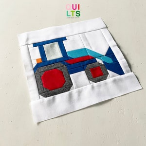 Könnte beinhalten: Ein weißer Stoffquadrat mit einem blauen, roten, grauen und türkisfarbenen Patchwork-Traktor-Design. Der Stoffquadrat ist von einem weißen Rand umgeben.