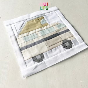 Op de afbeelding: Een wit vierkant van stof met een beige, grijs en blauw patchwork ontwerp van een camper. De stof is met een witte rand aan elkaar gestikt.