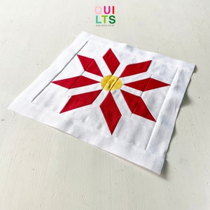 Op de afbeelding: Een rood en wit quiltblok met een geel centrum, met een stervormig ontwerp. Het blok is op een witte achtergrond. "QUI LTS AND NICE STUFF" staat in de linkerbovenhoek.