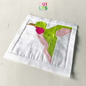Peut inclure: Un carré de tissu blanc avec un motif de colibri vert et rose. Le tissu est matelassé et a une bordure blanche. Le texte "OUI LTS AND NICE STUFF" est imprimé dans le coin supérieur gauche.