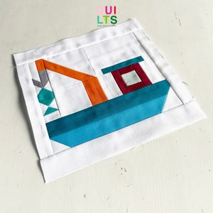 May include: A white fabric square with a colorful patchwork design of a boat. The boat is made of teal, orange, gray, and burgundy fabric. The text "QUI LTS AND NICE STUFF" is printed in the top left corner.