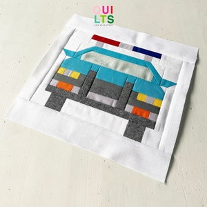 May include: A blue and gray patchwork quilt block depicting a car with a red and blue light on top. The car has yellow headlights and orange taillights. The quilt block is surrounded by a white border.