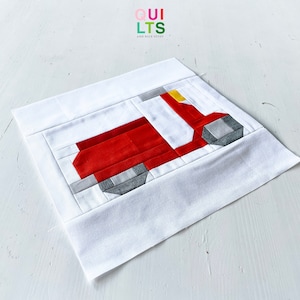 May include: A red and gray patchwork quilt block depicting a scooter. The scooter has a yellow handlebar and a white background.