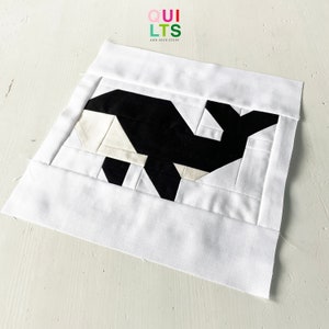 May include: A black and white whale quilt block with a white background. The quilt block is made up of various geometric shapes.