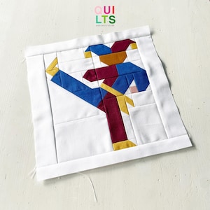 Könnte beinhalten: Ein quadratischer Quiltblock aus Stoff mit einem zusammengesetzten Design einer tanzenden Narrenfigur. Der Narr besteht aus blauen, kastanienbraunen und goldenen Stoffsegmenten auf weißem Grund. Der Text "QUILTS AND NICE STUFF" steht oben.