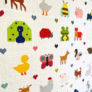 May include: A white quilt featuring a variety of colourful animal and insect designs. The quilt includes a horse, goose, bee, pig, peacock, ladybug, frog, fox, goat, duck, butterfly, chicken, cow, sheep, donkey, and a bluebird.