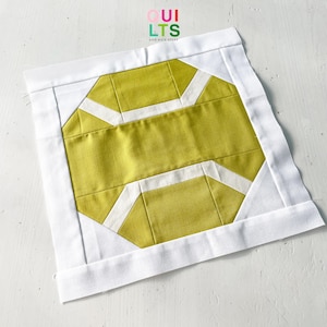 May include: A yellow and white quilt block with a geometric design. The block is surrounded by a white border. The text "QUILTS AND NICE STUFF" is printed in the top center of the image.