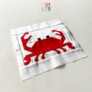 May include: A red and white striped crab quilt block with black eyes. The block is on a white background.