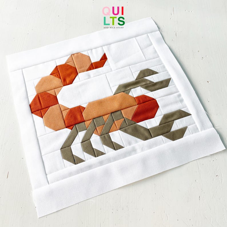 May include: A quilted square featuring a scorpion design in shades of orange, brown, and gray. The scorpion is centered on a white background with a white border. The text "QUILTS AND NICE STUFF" is in the upper right corner.