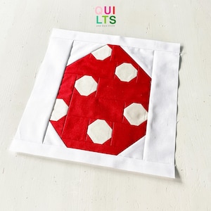 May include: A square quilt block with a red mushroom design and white polka dots, set within a white border. The text "QUILTS AND NICE STUFF" is visible in the upper right corner.