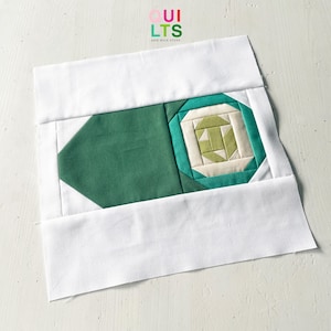 Könnte beinhalten: Ein im Entstehen begriffener Patchwork-Block mit einem geometrischen Muster. Das Design verwendet grüne, cremefarbene und weiße Stoffe. Der Text "QUILTS AND NICE STUFF" ist in der oberen rechten Ecke sichtbar.