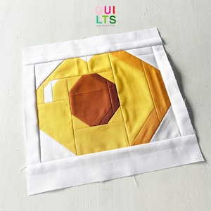 Könnte beinhalten: Ein geometrischer Quiltblock mit einem zentralen braunen Achteck, umgeben von gelben und orangen Formen und einem weißen Rand. Der Text "QUILTS" und "AND NICE STUFF" ist in der oberen rechten Ecke sichtbar.