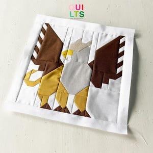 Könnte beinhalten: Ein weißer Stoffquadrat mit einem braunen, weißen und gelben Patchwork-Design eines Greifs. Der Stoffquadrat hat einen weißen Rand. Der Text "QUI LTS AND NICE STUFF" ist in der oberen linken Ecke gedruckt.