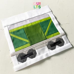 Könnte beinhalten: Ein Patchwork-Stoffblock mit geometrischem Design. Er zeigt Grün-, Grau- und Weißtöne mit einem schwarzen Akzent. Der Text "QUILTS AND NICE STUFF" ist sichtbar. Wahrscheinlich Teil eines größeren Quiltprojekts.
