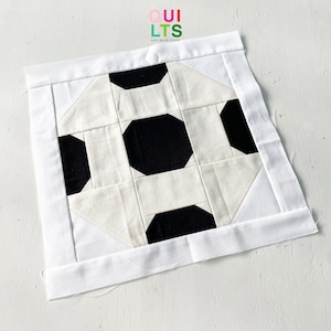 May include: Black and white quilt block with a geometric design. The block is made of fabric squares sewn together to create a pattern resembling a soccer ball.