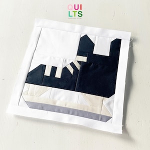 May include: A handmade quilt block featuring a stylized black and white sneaker design. The block is framed with a white border and includes the text "QUILTS AND NICE STUFF" in the upper right corner. The sneaker design incorporates geometric shapes.