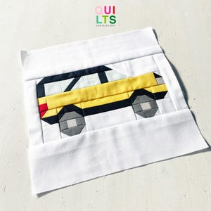 May include: A fabric quilt block featuring a yellow taxi cab design. The cab has black and white details, gray wheels, and a red taillight. The block is set against a white background, with the text "QUILTS AND NICE STUFF" in the upper right corner.