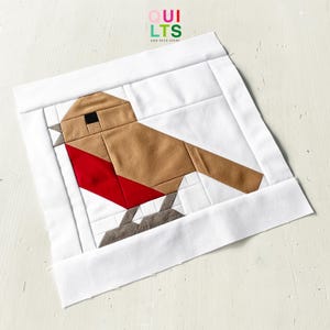 May include: A patchwork quilt block depicting a robin. The bird is rendered in brown, red, and grey fabrics, set against a white background. The block is framed with a white border. The text "QUILTS AND NICE STUFF" is in the upper right corner.