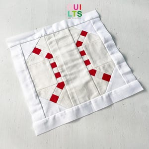 May include: A square, handmade quilt block featuring a candy cane design. The block is primarily white with red accents, and a white border. The text "QUILTS AND NICE STUFF" is in the upper left corner.