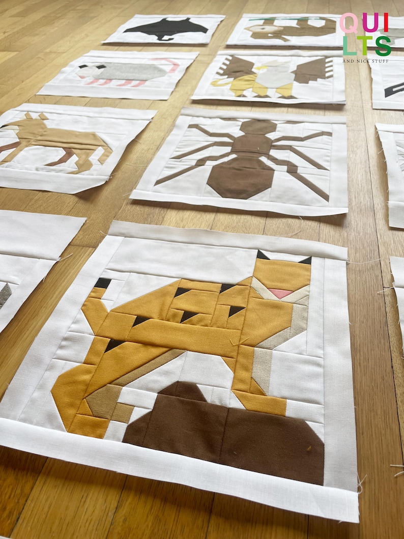 May include: A set of 10 unfinished quilt blocks featuring various animal designs. The blocks are made of white fabric with colourful fabric appliques. The animals include a bat, a raccoon, a squirrel, a bird, an ant, a lynx, a deer, a fish, a turtle, and a frog.