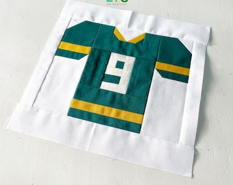 Peut inclure: Un bloc de courtepointe de maillot de football vert et or avec le numéro 9 sur le devant. Le bloc est entouré d'une bordure blanche.