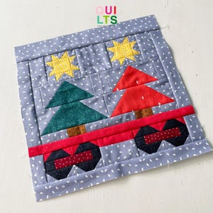 Könnte beinhalten: Ein gesteppter Block mit einem roten Lastwagen, der einen grünen und roten Weihnachtsbaum hinten drauf hat. Der Lastwagen hat schwarze Räder und eine rote Ladefläche. Der Hintergrund ist ein hellblauer Stoff mit weißen Schneeflocken.