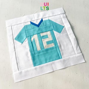 May include: A white fabric square with a blue and white jersey applique in the center. The jersey has the number "12" on the front.