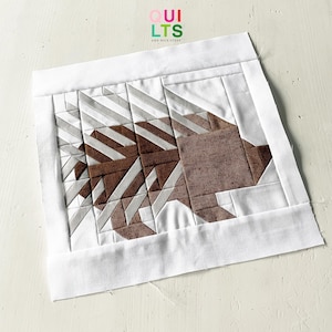 Puede incluir: Un cuadrado de tela blanco con un diseño geométrico marrón y blanco de un erizo. El cuadrado de tela tiene un borde blanco. El texto "OUI QUILTS AND NICE STUFF" está en la esquina superior izquierda de la imagen.