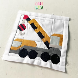 May include: A quilted square featuring a yellow, black, gray, and red crane design. The crane is set against a white background with a white border. The text "QUILTS AND NICE STUFF" is in the upper right corner.
