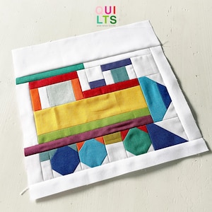 Könnte beinhalten: Ein farbenfroher, geometrischer Quiltblock mit einem Zug-Design. Der Quiltblock besteht aus verschiedenen Stoffstücken in Gelb-, Rot-, Blau-, Grün- und Lilatönen. Der Text "QUILTS AND NICE STUFF" ist oben rechts zu sehen.