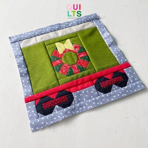 May include: A quilted Christmas-themed placemat featuring a central green panel with a wreath design. The wreath is red and green, with a yellow bow. The placemat has a red stripe and a blue border with white polka dots. The text "QUILTS AND NICE STUFF" is in the upper right corner.