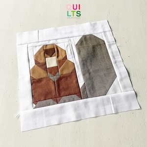 Könnte beinhalten: Ein brauner und weißer Patchwork-Quiltblock mit einem grauen Stoffrechteck daneben. Der Quiltblock ist von einem weißen Rand umgeben. Der Quiltblock besteht aus verschiedenen geometrischen Formen. Der Quiltblock ist ein modernes Design. Der Quiltblock ist eine großartige Ergänzung für jedes Quiltprojekt.